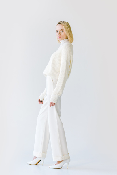 side view of beautiful stylish blonde woman in white clothes looking at camera on white - Fotoğraf, Görsel