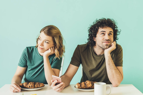 улыбающаяся пара с помощью смартфона и глядя в сторону во время завтрака вместе
 - Фото, изображение
