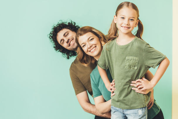 ευτυχείς γονείς με χαριτωμένη μικρή κόρη φορώντας t-shirts και να χαμογελά στη φωτογραφική μηχανή  - Φωτογραφία, εικόνα