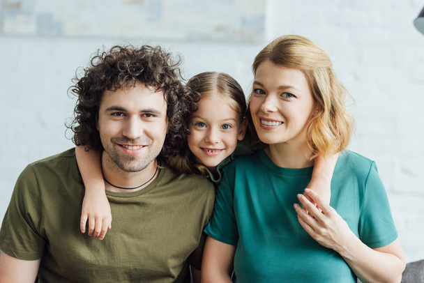 happy family with one child embracing and smiling at camera - Foto, afbeelding