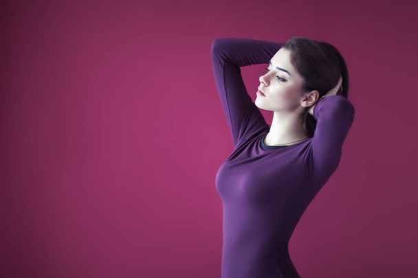 Portrait of sexy beautiful woman in purple dress posing on pink background with copy space - 写真・画像