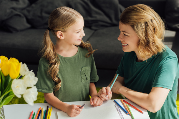 happy mother and daughter drawing together and smiling each other at home  - Photo, Image
