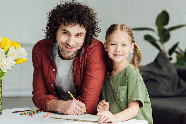happy father and daughter drawing together and smiling at camera at home - Fotó, kép