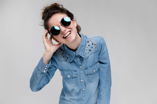 Young brunette caucasian girl with bun hairstyle wearing round sunglasses isolated on gray - Foto, Imagem