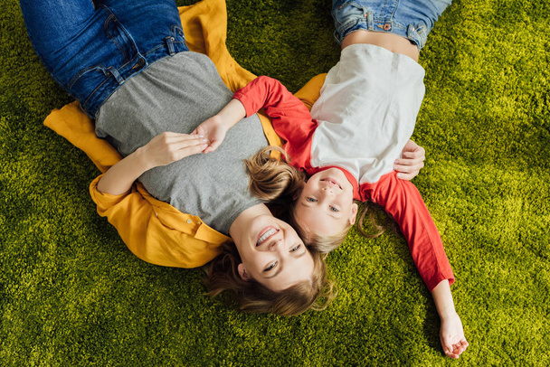top view of happy mother and daughter lying together and smiling at camera  - Фото, зображення