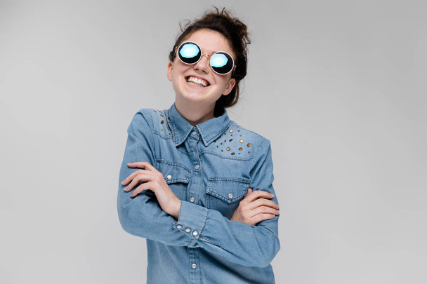 Young brunette caucasian girl with bun hairstyle wearing round sunglasses isolated on gray - Foto, imagen