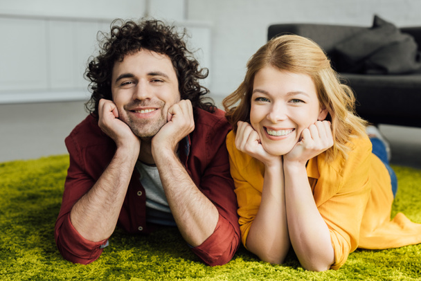 beautiful happy couple lying on carpet and smiling at camera at home - Foto, immagini