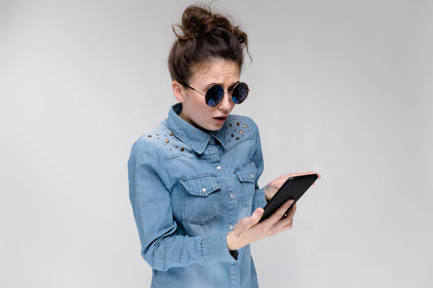 Young brunette caucasian girl with bun hairstyle in sunglasses using smartphone isolated on gray - Photo, Image