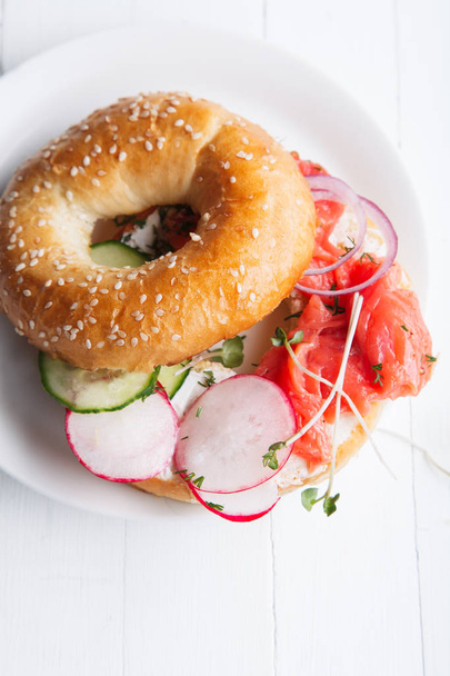 bagel with salmon fish and cream cheese with cucumber and fresh radish slices on white plate  - Foto, imagen