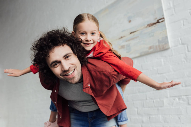 happy father piggybacking cute little daughter and smiling at camera at home - Foto, immagini