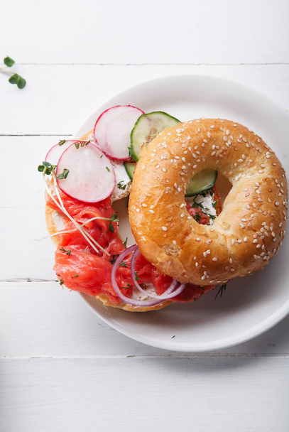 bagel with salmon fish and cream cheese with cucumber and fresh radish slices on white plate  - Φωτογραφία, εικόνα