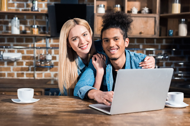 portrait of smiling multiracial couple with laptop together in kitchen at home - Photo, image