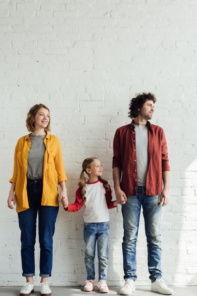 щаслива сім'я з однією дитиною тримає руки, стоячи разом і озираючись
 - Фото, зображення
