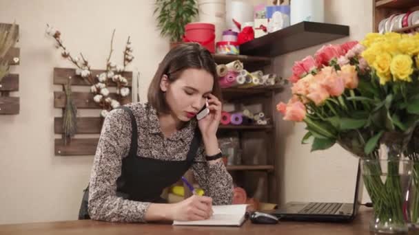 Jovem dona mulher de loja de flores está encomendando bens por telefone e escrita
 - Filmagem, Vídeo