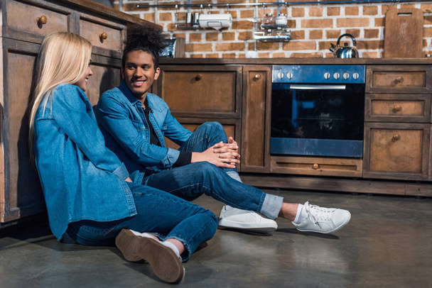 happy interracial couple sitting on floor in kitchen at home - Photo, Image