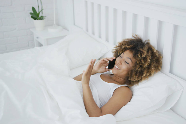 Mujer contenta hablando por teléfono en la cama
 - Foto, imagen
