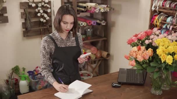 Salesgirl de studio de fleurs compte sur une calculatrice smartphone et écriture
 - Séquence, vidéo