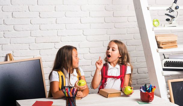 School time of girls. Little girls eat apple at lunch break. Happy school kids at lesson in september 1. Friendship of small sisters in classroom at knowledge day. Back to school and home schooling. - Φωτογραφία, εικόνα