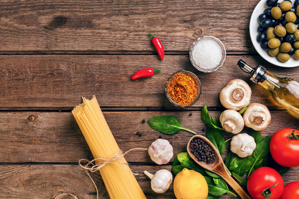 Nudelzutaten - Tomaten, Olivenöl, Knoblauch, italienische Kräuter, frisches Basilikum, Salz und Spaghetti auf einem hölzernen Hintergrund mit Kopierraum, horizontal, Ansicht von oben - Foto, Bild