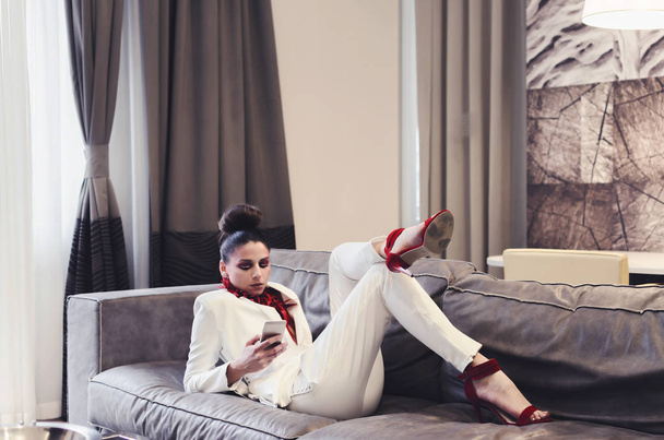 young woman in white suit and red necklace using smartphone - Фото, зображення