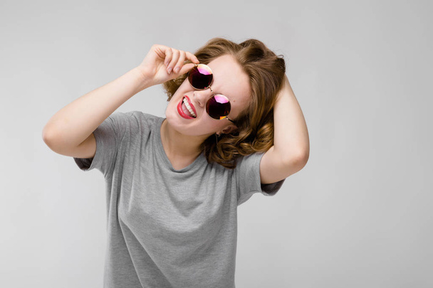 Fényvisszaverő napszemüveget, szürke háttér gyönyörű vörös hajú boldog fiatal nő portréja - Fotó, kép