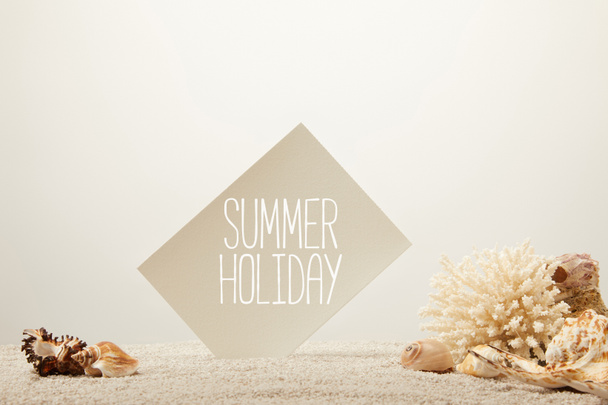 close up view of coral, seashells and card with summer holiday lettering on sand on grey background - 写真・画像