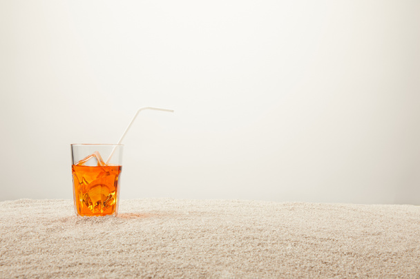 close up view of refreshing cocktail with ice and straw on sand on grey background - Zdjęcie, obraz