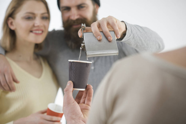 Men, woman on smiling faces, white background. Communication, friendship, fun. Guys pouring cup with alcohol out of flask. Company of cheerful friends spend leisure with drinks. Fun and drink concept. - 写真・画像