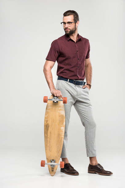 modischer Skater posiert mit Longboard, isoliert auf grau - Foto, Bild
