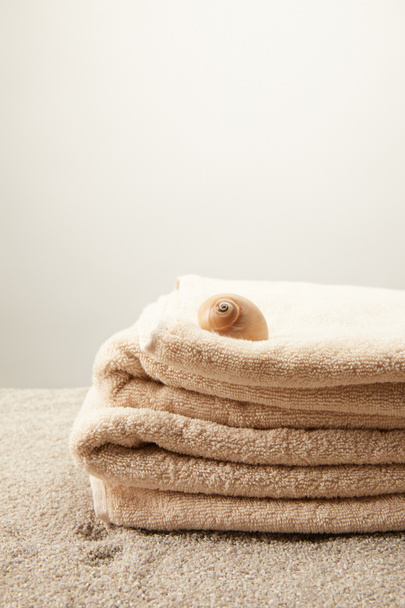 Nahaufnahme eines Stapels Handtücher mit Muschel auf Sand vor grauem Hintergrund - Foto, Bild