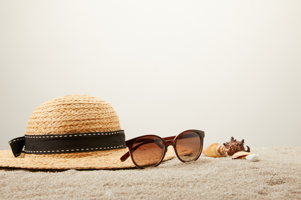 close up view of straw hat, sunglasses and seashells on sand on grey backdrop - Photo, Image