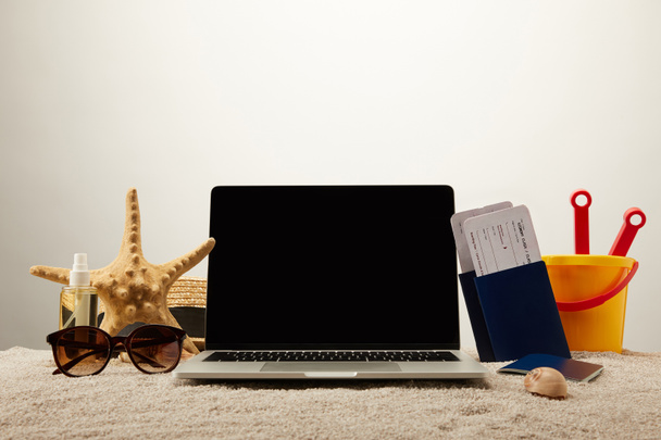 close up view of laptop with blank screen, sea star, sunglasses, passports with tickets and toy bucket on sand on grey background - Photo, Image