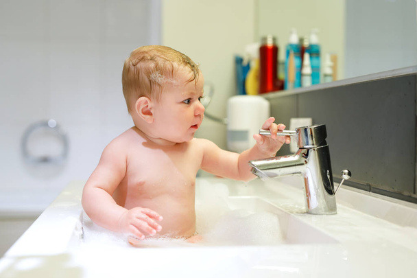 Bebê adorável bonito tomando banho na pia de lavagem e brincando com água e espuma - Foto, Imagem