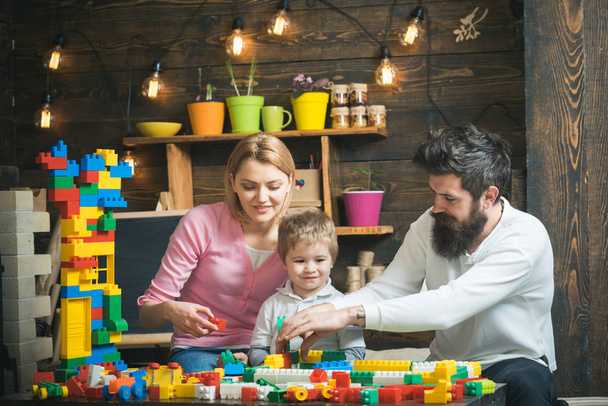 Father, mother and cute son play with constructor bricks. Family on busy face spend time together in playroom. Educational game concept. Kid with parents play with plastic blocks, build construction. - Foto, Bild