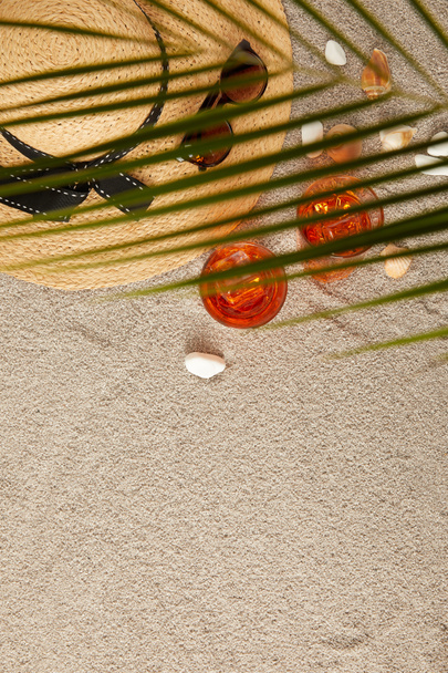 top view of arranged straw hat, sunglasses, cocktails, seashells on sand and palm leaf - Fotoğraf, Görsel