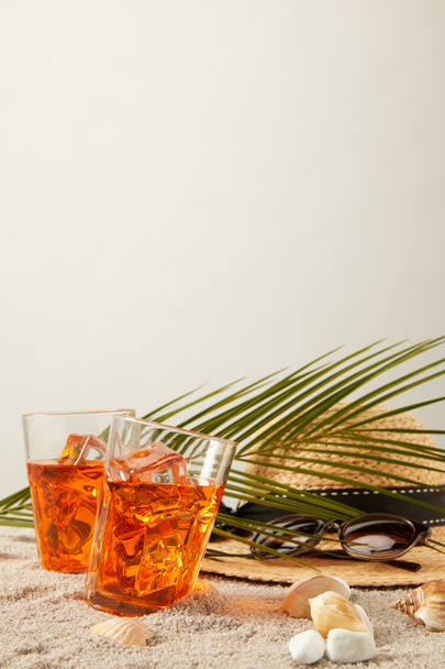 close up view of straw hat, cocktails, seashells, sunglasses and palm leaf on sand on grey backdrop - Foto, imagen