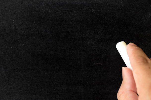 Hand hold white chalk on blackboard textured background - Photo, Image