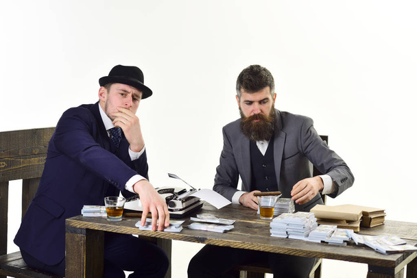 Illegal business concept. Company engaged in illegal business. Men sitting at table with piles of money and typewriter. Businessmen discussing illegal deal while drinking and smoking, white background - Photo, Image
