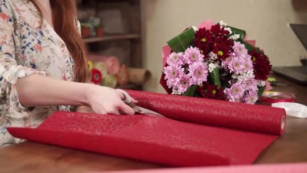 Frauenhände schneiden Geschenkpapier von einer Rolle auf einem Tisch im Blumenatelier - Filmmaterial, Video
