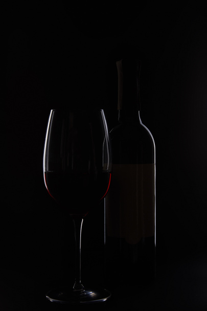 closeup shot of bottle and glass with red wine isolated on black background - Foto, Imagen