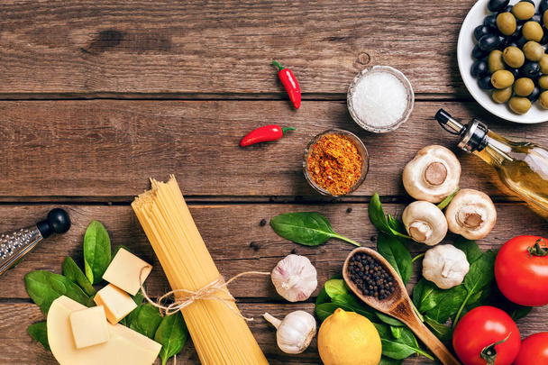 Pasta ingredients - tomatoes, olive oil, garlic, italian herbs, fresh basil, salt and spaghetti on a wooden background with copy space, horizontal, top view - Photo, Image
