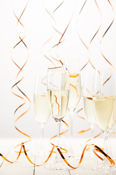 Copas de champán con serpentinas doradas en mesa de madera blanca, concepto de vacaciones
 - Foto, Imagen