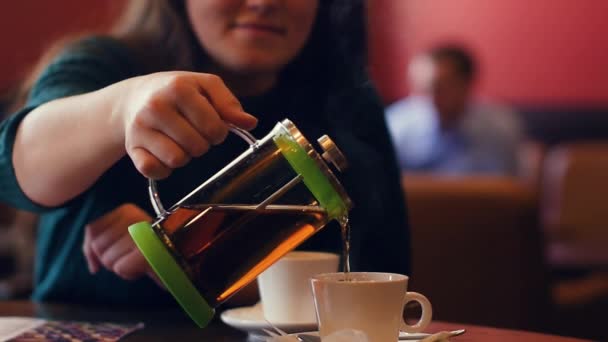 a young woman pours hot tea from a glass teapot into the cup at a slow pace. - Video