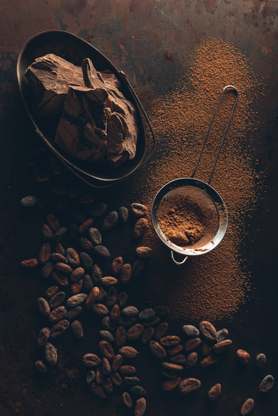 delicious chocolate pieces, cocoa beans, powder and sieve on dark surface  - Photo, Image