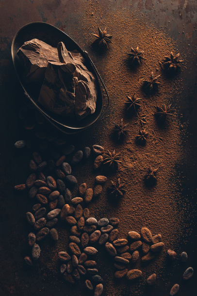 vista superior de granos de cacao, anís estrellado, trozos de chocolate y cacao en polvo en la superficie oscura
 - Foto, Imagen