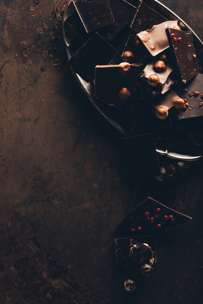 vista superior de dispostas sortidas deliciosas peças de chocolate com nozes na superfície escura
 - Foto, Imagem