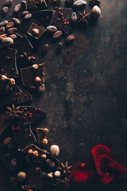 το Top view λαχταριστής σοκολάτας με ξηρούς καρπούς, αστεροειδή γλυκάνισο και ροδοπέταλα στην σκοτεινή επιφάνεια - Φωτογραφία, εικόνα