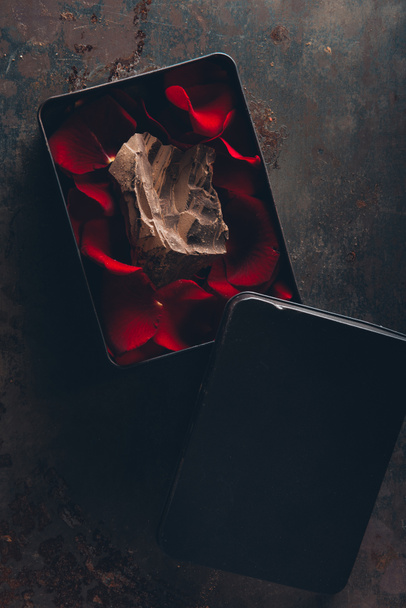 top view of box with red rose petals and gourmet piece of chocolate - Fotografie, Obrázek