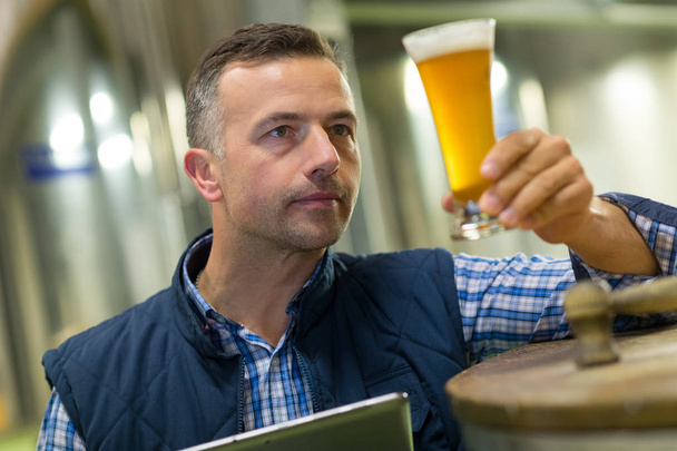handsome brewer in uniform tasting beer at the brewery - Zdjęcie, obraz
