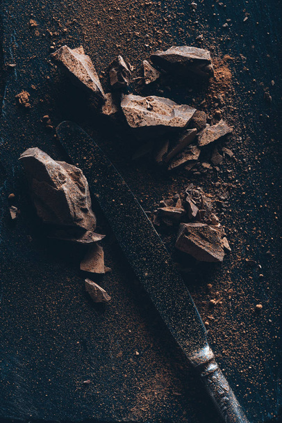 вид зверху вінтажний ніж, шоколадні шматочки та какао-порошок на темній поверхні
  - Фото, зображення